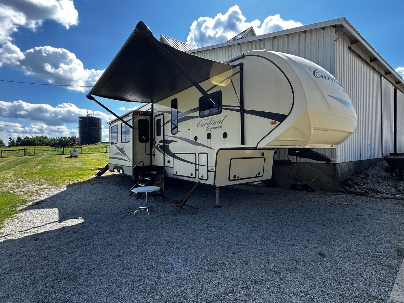 The Airbnb RV with its awning out, parked beside a white barn on the farm
